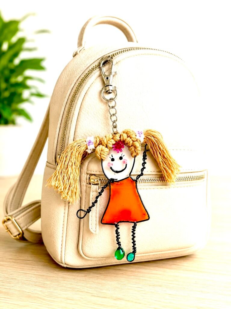 Bag Charm from the Mary-Anne Collection showing Cheeky Girl Character in an orange dress made with uv resin and hair tied in bunches attached to a small ladies ruck sack in cream colour